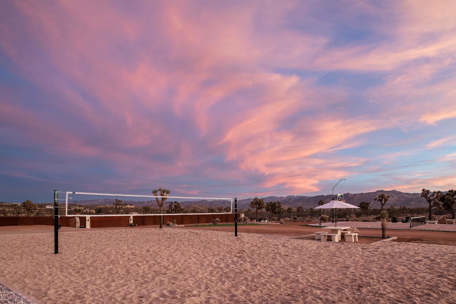 Private sand volleyball court under a pink sunset sky