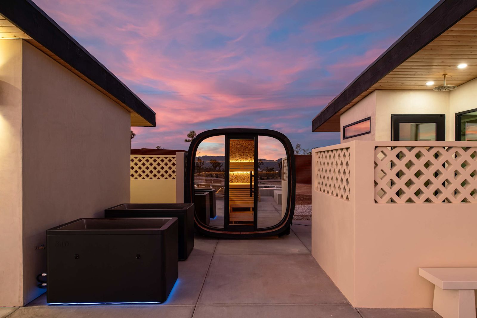 Finnish sauna pod and cold plunge tubs between the two homes at dusk
