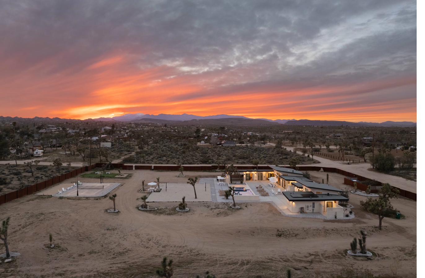Sandhouse aerial at fiery sunset — full estate with courts
